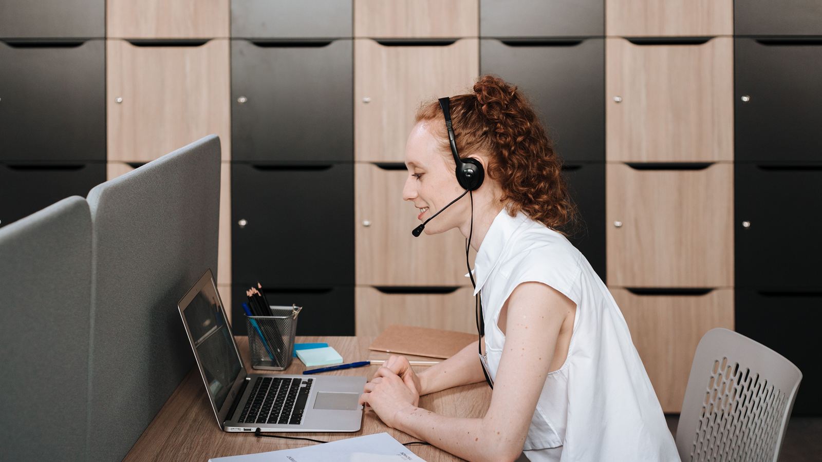 A woman with a headset smiling as she speaks to her laptop