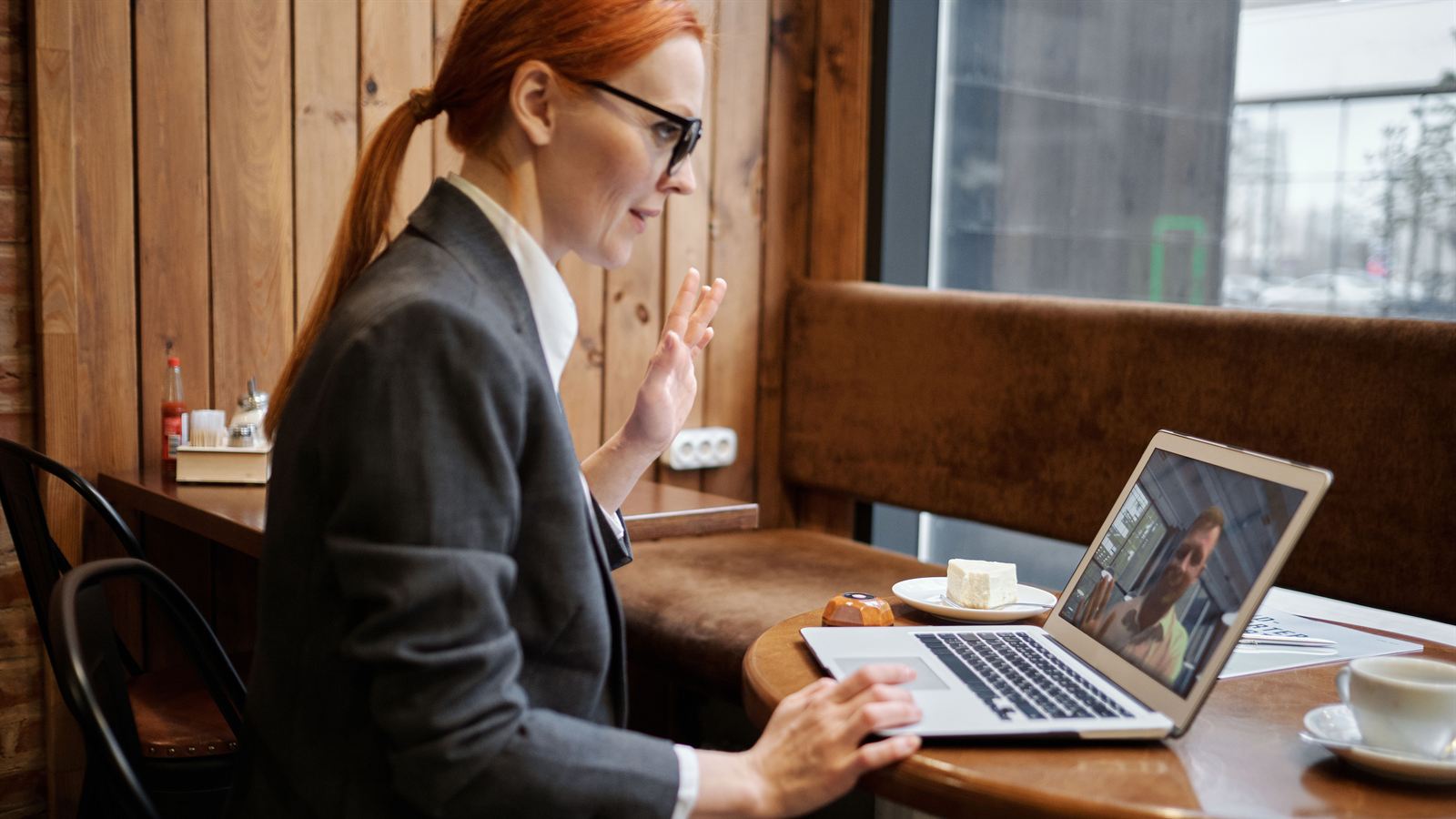 A woman in a blazer waving at someone on a laptop video call